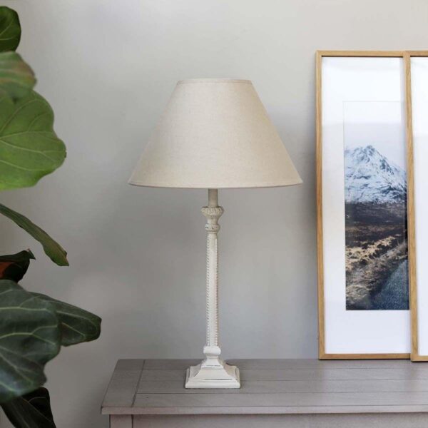Table lamp with light linen shade on a table next to a picture frame.
