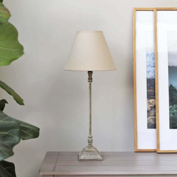 Natural thin table lamp with shade on a table next to a picture frame.