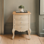 Juliette 3 Drawer Bedside in champagne with a natural wood top and three clear crystal handles, styled with a plant and book in a neutral bedroom setting.
