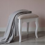 Romance white dressing table stool featuring sweeping French Rococo cabriole legs and a softly padded neutral seat, styled with a draped grey throw blanket against a pink striped wall.