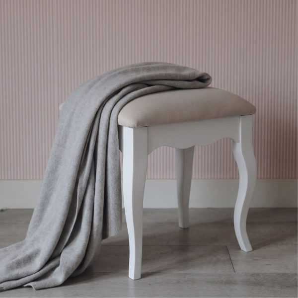 Romance white dressing table stool featuring sweeping French Rococo cabriole legs and a softly padded neutral seat, styled with a draped grey throw blanket against a pink striped wall.