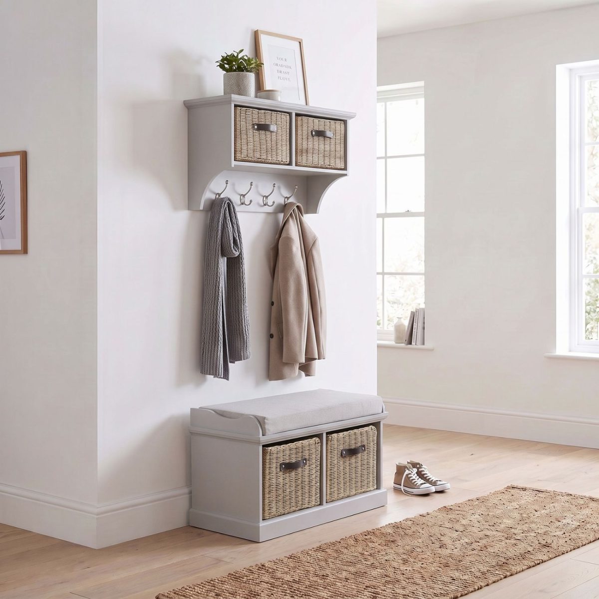 A truffle-coloured wall-mounted shelf unit displaying a framed print and potted plant on top, with two natural woven baskets featuring dark handles in its cubbies and four silver double-hooks holding a grey scarf and a beige coat. Directly below sits a matching truffle wooden storage bench topped with a light grey cushion, containing two larger natural woven baskets in its base. The furniture is styled in a bright hallway with light wood flooring, a woven runner rug, and a pair of canvas sneakers resting beside the bench.
