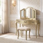 A French-inspired gold dressing table set with curved cabriole legs. The table features three drawers with dark handles, topped with a three-way mirror and paired with a cream upholstered stool.