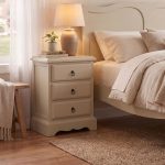 Romance beige bedside table with three smooth-running drawers, antique brass drop ring handles, and a curved sweetheart base.