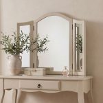 Romance tri fold vanity mirror featuring a gracefully arched top and a sturdy beige wooden frame atop a matching dressing table.