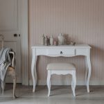 Romance white dressing table and stool set featuring French Rococo curved legs, a central drawer, and a padded seat, styled with an arrangement of rustic bottles against a striped pink wall.
